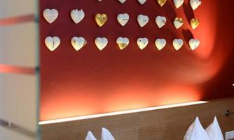 A cozy bedroom with two beds and elegant pillows. Numerous decorative hearts on a red background hang on the wall.