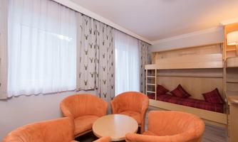 A cozy room with two orange chairs and a round table. In the background, there is a bunk bed with red cushions.