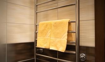 A towel hangs on a modern towel radiator in a bathroom. The walls are brightly tiled, creating a pleasant atmosphere.
