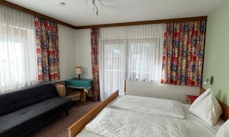 A bright bedroom with a double bed and a sofa. The windows are covered with curtains and the room feels cozy and inviting.
