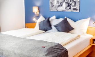 A modern bedroom with a large bed and cozy pillows. The walls are painted in a calming shade of blue, and there is stylish lighting.