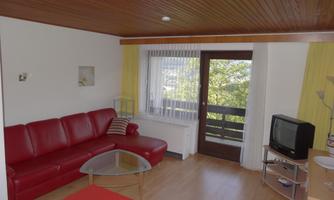 A modern living room with a red sofa and a glass table. Large windows provide plenty of light and a view outside.