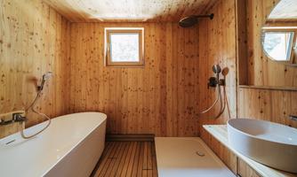 A modern wooden bathroom with a bathtub and a shower. Large windows provide plenty of natural light.