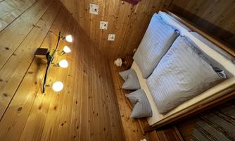 A cozy bedroom with wooden walls and a double bed. The clothing is light blue, and the lighting creates a warm atmosphere.
