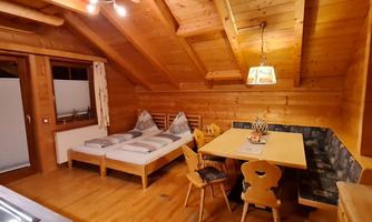 A cozy wooden porch with two single beds and a dining table. The walls and ceiling are made of wood, which creates a warm atmosphere.