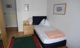 A simple bedroom with a single bed and a nightstand. There is a green carpet area and small wall pictures.