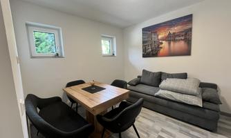 A cozy room with a gray sofa and a wooden dining table. A picture of a landscape at sunset hangs on the wall.