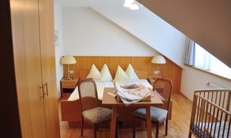 A cozy room with a double bed and two chairs at the table. The room has wooden flooring and a skylight that provides natural light.