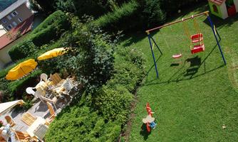 A beautiful garden with a play swing and a playhouse. There is also a seating area with umbrellas and chairs.