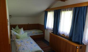 A cozy bedroom with two single beds and colorful bedding. Large windows let in plenty of sunlight and create an inviting atmosphere.