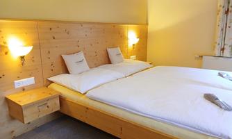 A cozy bedroom with a double bed and wooden nightstands. The walls are painted light and illuminated with warm light.