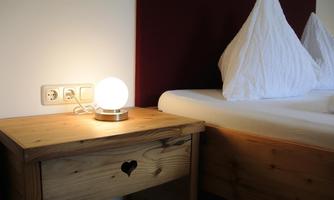 A cozy bedroom with a wooden nightstand and a round lamp. In the background, white pillows are visible on the bed.
