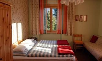 A cozy bedroom with a double bed and a single bed. Large windows with curtains let in a lot of light and offer a view outside.
