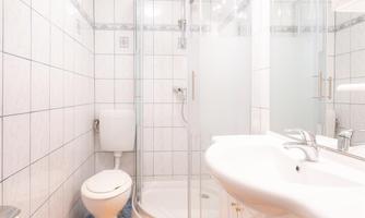 A modern bathroom with a shower and a toilet. The floor is fitted with a blue carpet and an orange bath mat.