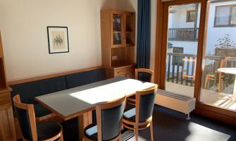 A cozy dining area with a table and wooden chairs. Large windows provide plenty of light and offer views of the balcony.