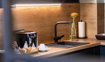 A modern kitchen with wooden surfaces and sleek black appliances. Fresh flowers and a plate of pastries are on the countertop.