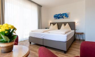 A modern room with a double bed and cozy red armchairs. A small table with a blooming plant completes the decor.