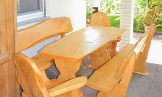 A rustic wooden table with matching benches is situated on a terrace. The area is surrounded by a green garden, creating an inviting atmosphere.