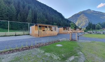 Wooden cabins in a picturesque landscape with mountains in the background. Lots of greenery surrounds the area, perfect for a peaceful stay in nature.