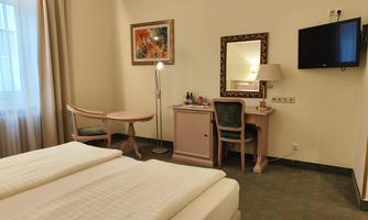 A cozy hotel room with two beds, a table, and a chair. A flat-screen TV and a mirror hang on the wall.