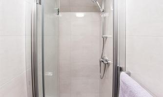 A modern shower cubicle with glass doors and a bright interior. A towel hangs on the wall next to it.