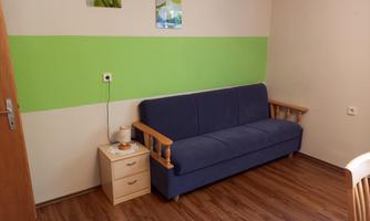A living room with a blue sofa and a small bedside table. There is a green stripe on the wall and two pictures are hanging.