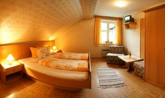 A cozy bedroom with two beds and a small table. The walls are decorated with a light pattern and the light is warm and inviting.