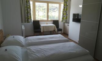 A bright room with two single beds and a table. Large windows overlooking nature.