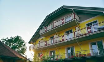 A bright yellow building with several balconies. In the background, there are trees and a clear sky.