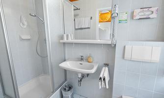 A modern bathroom with a shower and sink. The walls are tiled in light blue, and there are towels and toiletries.