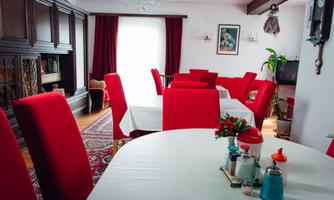 An inviting dining area with red chairs and a large table. In the background, there are windows with curtains and decorative elements.