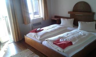 A simple bedroom with two beds and light curtains. Sunlight streams through the window, creating a cozy atmosphere.