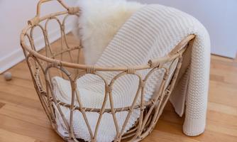 A basket made of rattan with soft, white fabric and a blanket. The bottom is made of wood, creating a cozy atmosphere.