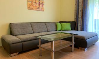 A cozy living room with a modern gray sofa and a glass table. In the background, a picture of a beach landscape hangs on the wall.