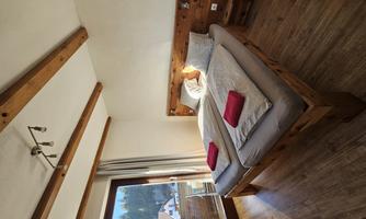A cozy bedroom with a wooden bed and two separate mattresses. The large windows provide plenty of daylight and a view of nature.