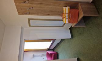A bright hallway with a wooden panel that has coat hooks attached. On a bench lies an orange bag with striped towels.