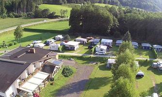 A campsite with motorhomes and pitches in a green environment. In the background, forests and hills can be seen.
