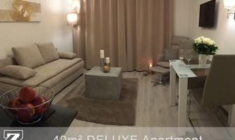 A modern living room with a comfortable sofa, a coffee table, and a dining area. The warm lighting creates an inviting atmosphere.