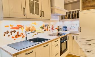 A modern kitchen with bright cabinets and a spacious countertop. The colorful background showcases a variety of foods and spices.