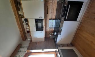 A modern kitchen with white cabinets and a black countertop. Wood paneling and a window create a cozy atmosphere.
