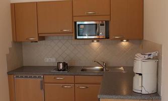 A modern kitchen with wooden cabinets and a bright workspace. It is equipped with kitchen utensils and appliances.