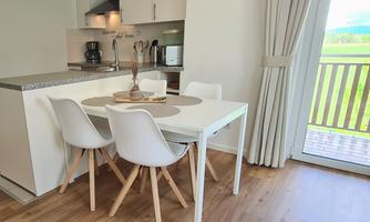 A modern dining room with a white table and four chairs. The large window front lets in plenty of daylight.