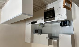 A modern kitchen with bright cabinets and a cooking range. In the background, a refrigerator and a small bar can be seen.