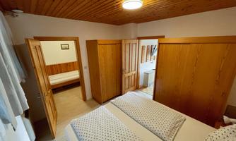 A cozy room with wooden paneling and two beds. In the background, there is an additional bed and a wardrobe.