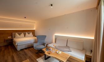 A modern room with wooden floors and minimalist design. There is a cozy bed, a chair, and a table with refreshments.
