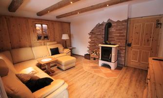 A cozy living room with wooden walls and a modern fireplace. There is a light sofa, a low table, and a window that lets in daylight.