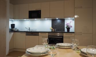 Modern kitchen with elegant white cabinets and a dark work area. The table is set with plates and glasses, and a bouquet of flowers is on the countertop.