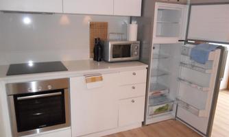 A modern kitchen with white cabinets and an elegant cooktop. The refrigerator is open and shows a neat interior.
