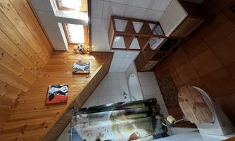 A rustic bathroom with wooden ceilings and tiled floor. There is a bathtub with a shower, a toilet basin, and a storage cabinet.