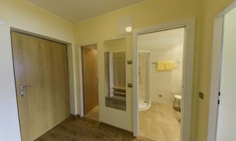 A bright hallway with an open bathroom door. The walls are painted in a soft yellow, and there is a shower in the background.